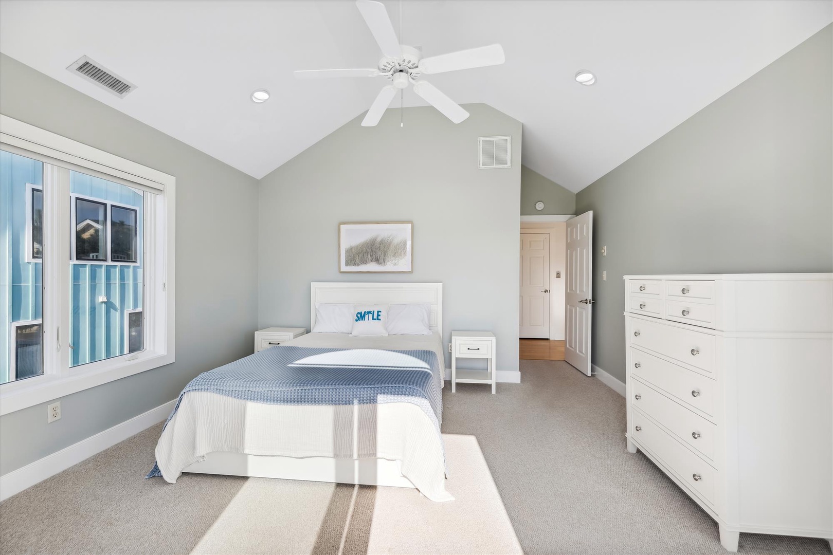 You'll love this serene bedroom with vaulted ceilings, a cozy white bed, ceiling fan, and plenty of storage. Soft gray-green walls and natural light create a calming retreat.