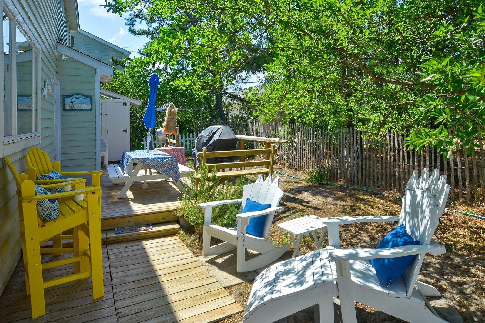 A sunny backyard retreat with colorful Adirondack chairs, a relaxing hammock, and picnic seating where you can unwind under the trees and enjoy the coastal breeze.