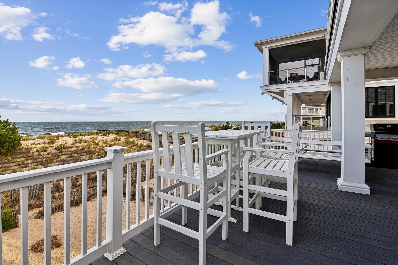 A pristine beachfront property featuring elevated decks with ocean views. Situated directly on sandy dunes with unobstructed coastal access under open skies.