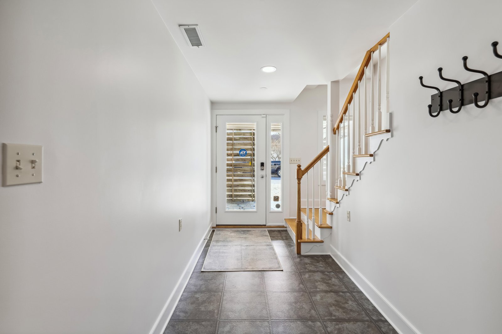 Step inside to find a bright, welcoming entryway with tile flooring, a sturdy wooden staircase, and convenient coat hooks—your first taste of the care and comfort waiting throughout your stay.
