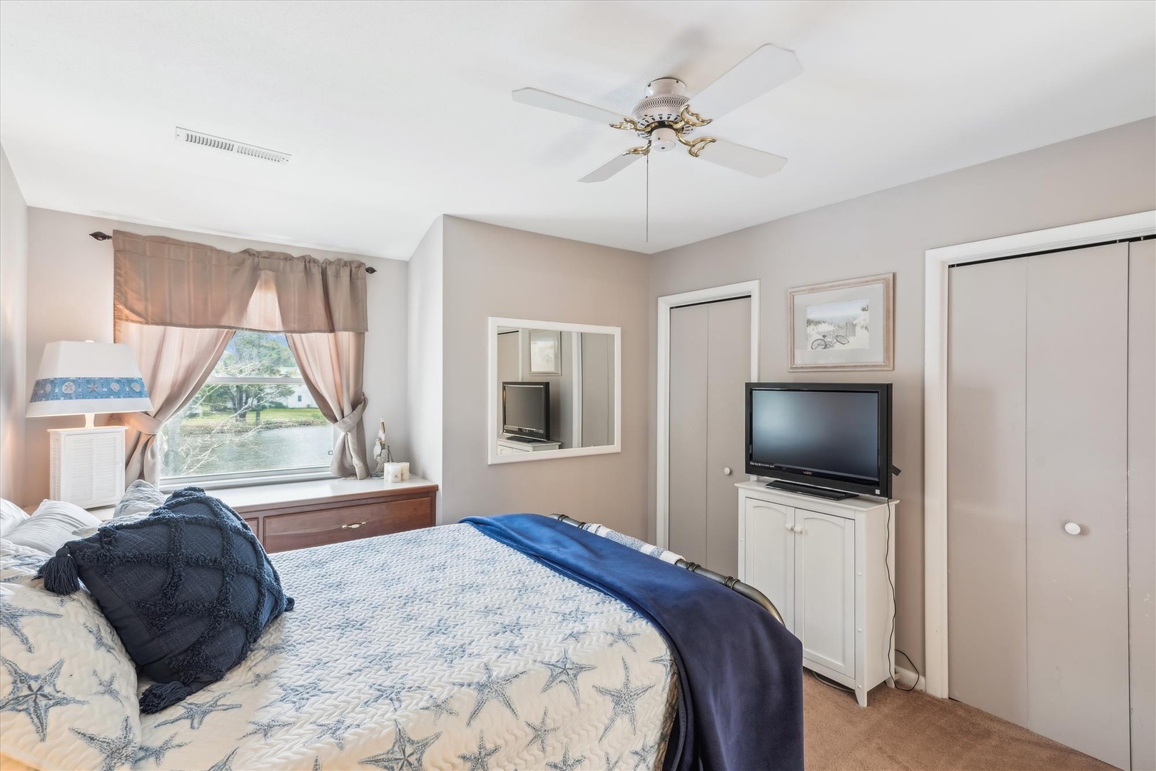 Your private bedroom features a ceiling fan, flat-screen TV, and scenic water views through the large window—a cozy retreat after a day of exploring.