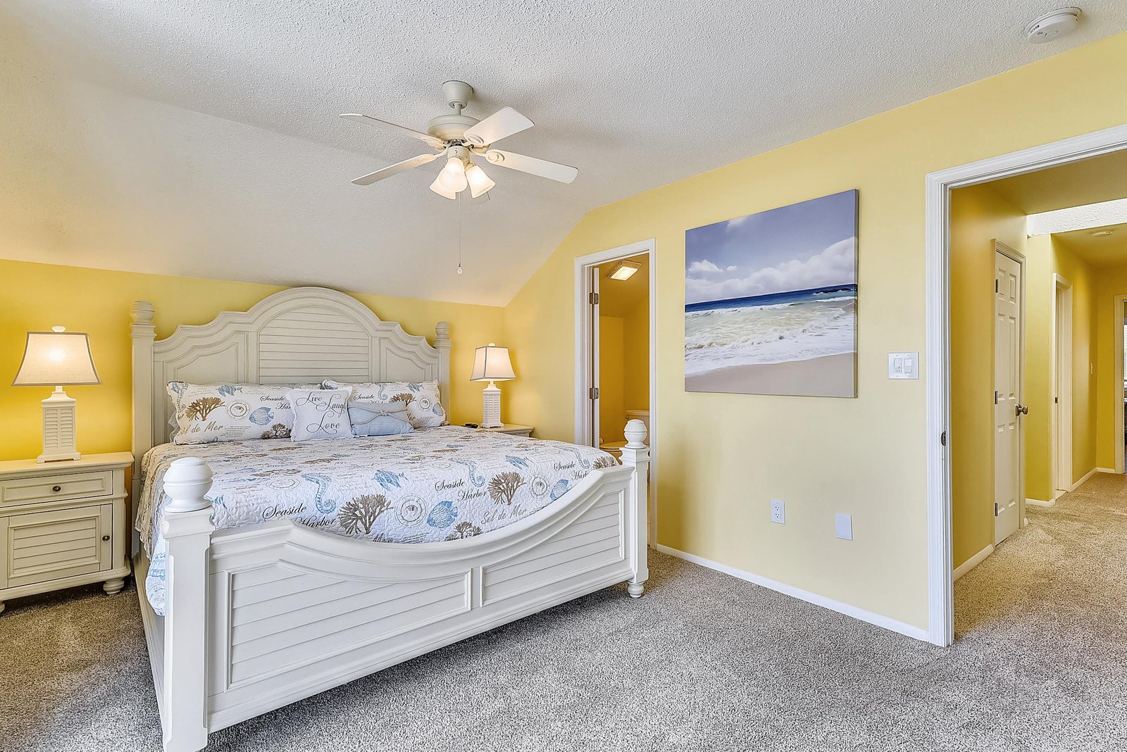 Sink into your plush bed surrounded by cheerful coastal décor and soft lamplight, where restful nights come naturally beneath the gentle whir of the ceiling fan.