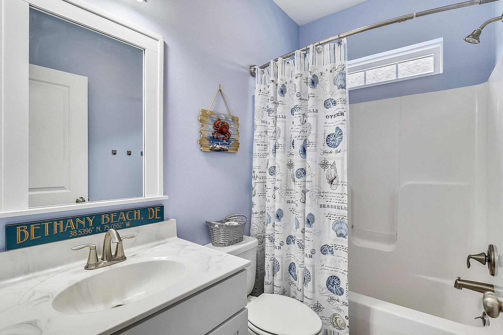 Step into a bright coastal bathroom with crisp blue walls and charming beach-themed touches. Crisp linens, a full tub-shower combo, and thoughtful beach decor welcome you after a day by the shore.