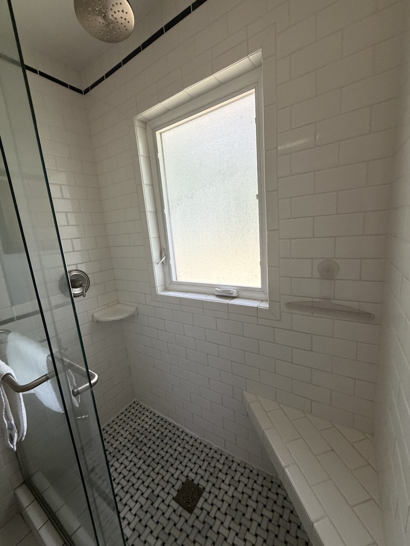 Natural light floods your private bathroom through the skylight, creating a bright and airy atmosphere with elegant white tile and modern fixtures that make your daily routine feel like a spa retreat.
