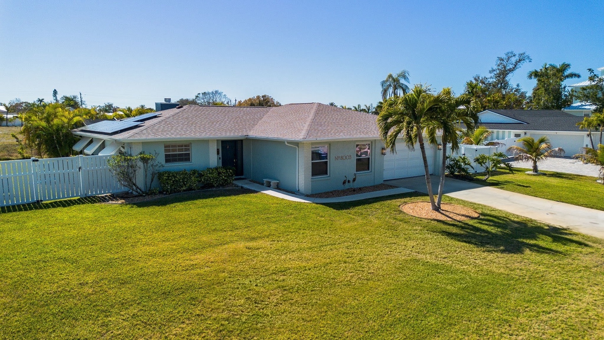 Charming coastal home features spacious lawn and tropical palms in peaceful residential neighborhood.