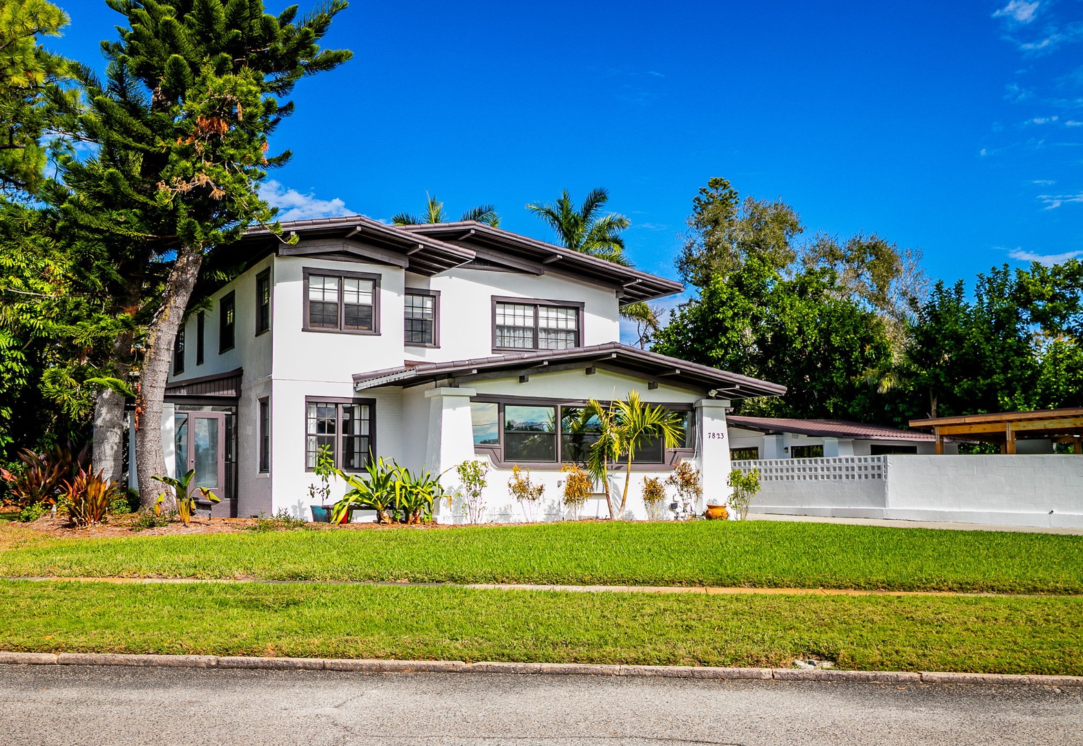Charming two-story vacation home nestled among tropical palms and lush greenery on a quiet residential street.