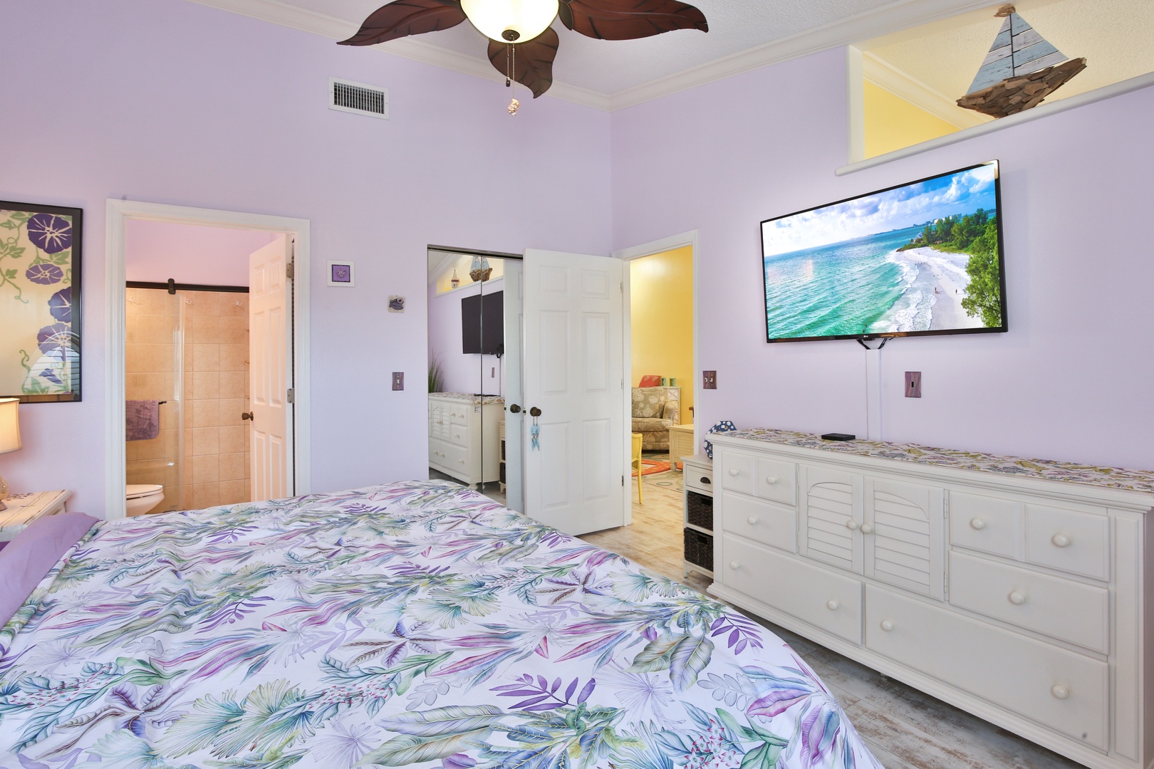 Unwind in this serene bedroom with calming coastal colors, ceiling fan, and tropical-themed linens inviting restful sleep after beach days.