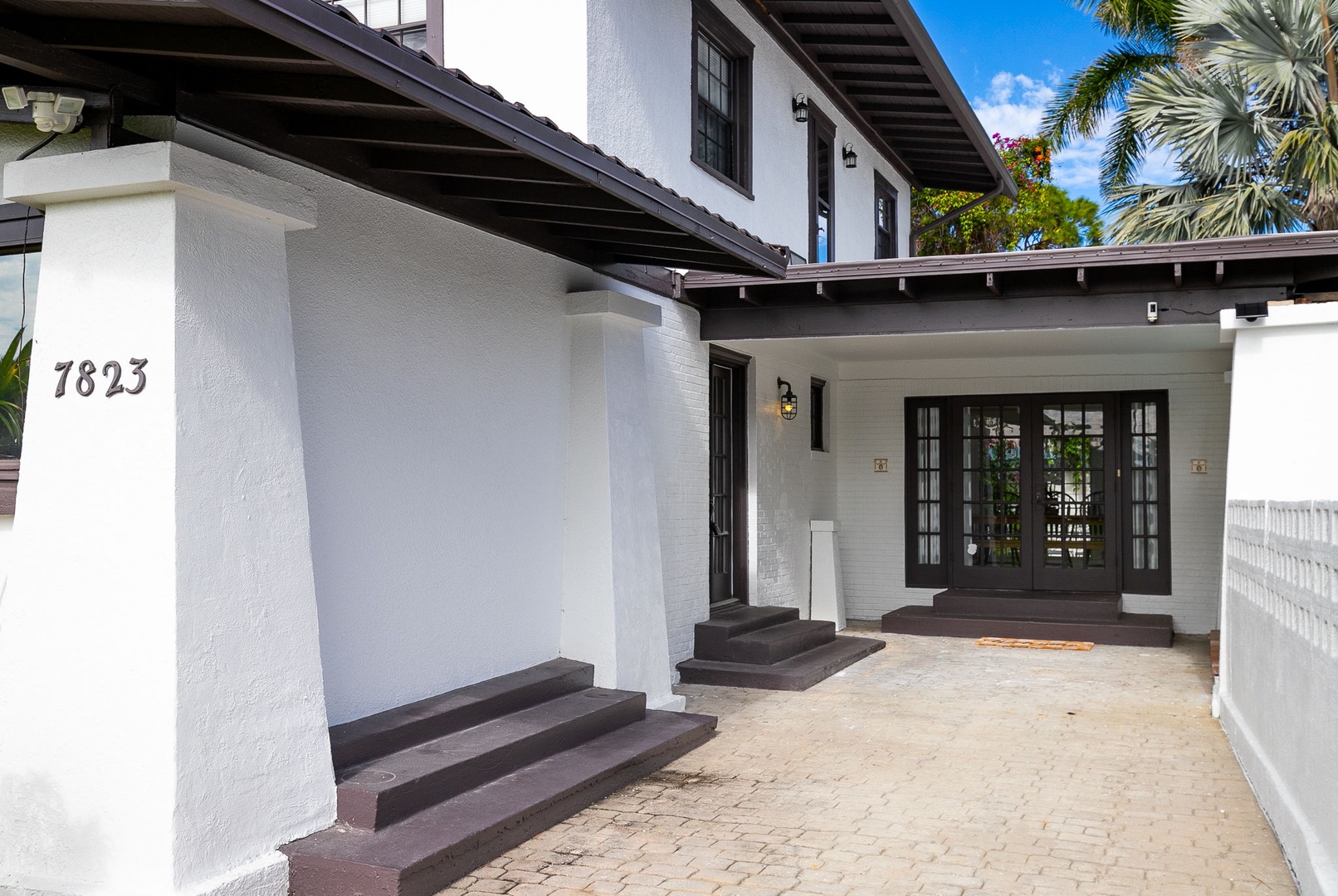 Elegant white colonial-style building with covered entrance featuring dark trim, tropical landscaping, and welcoming architectural details.