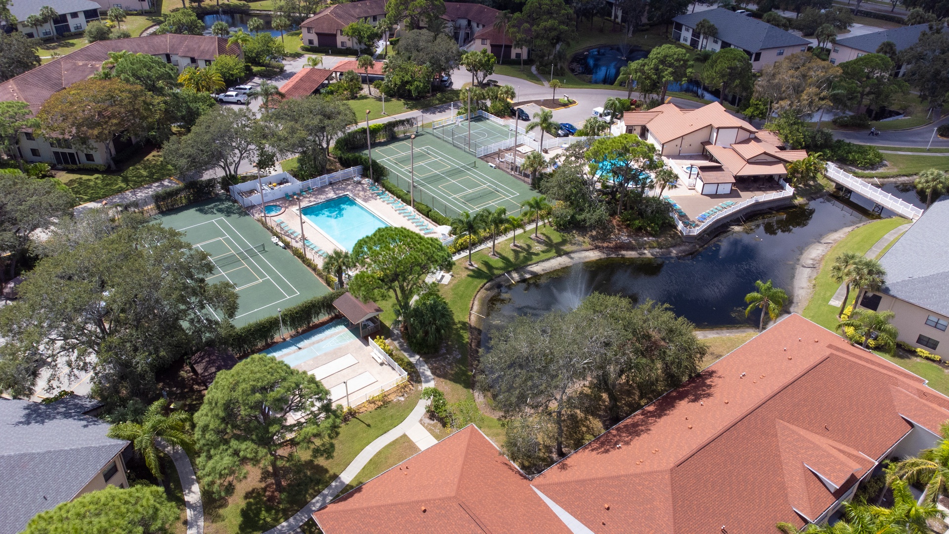 Resort community featuring tennis court, swimming pool, and peaceful lake surrounded by landscaped grounds in a quiet residential neighborhood.