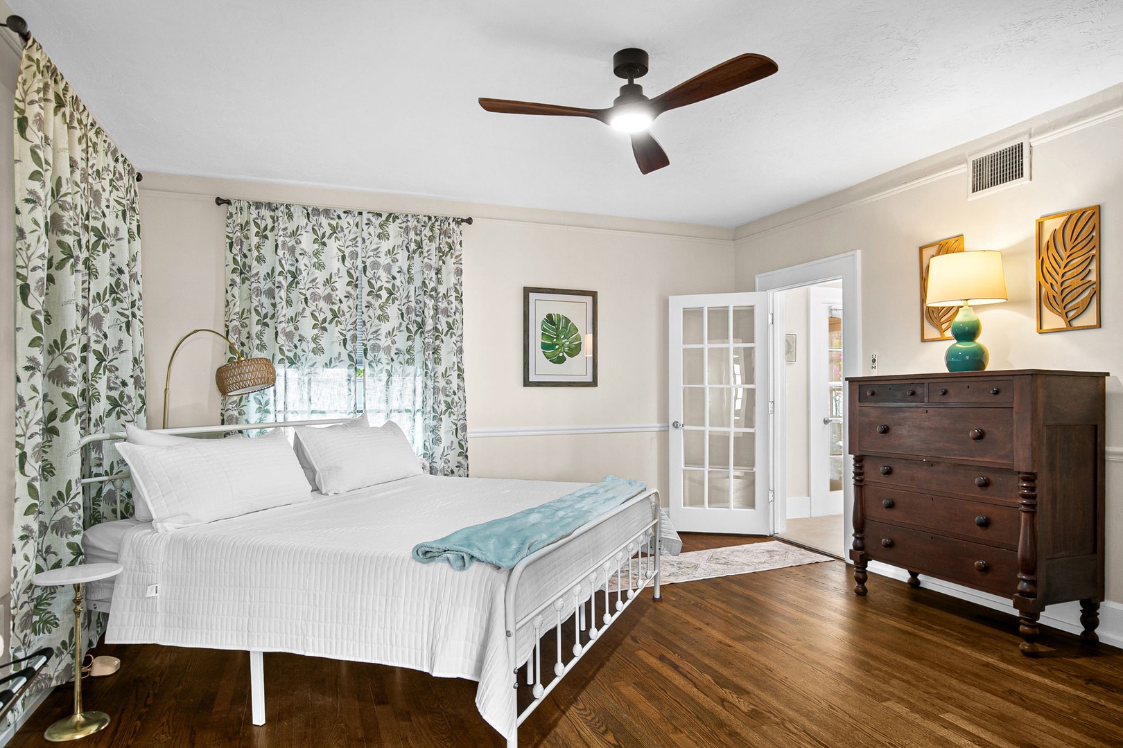 Unwind in your serene bedroom featuring leafy botanical prints and rich hardwood floors, where the ceiling fan keeps you comfortable.