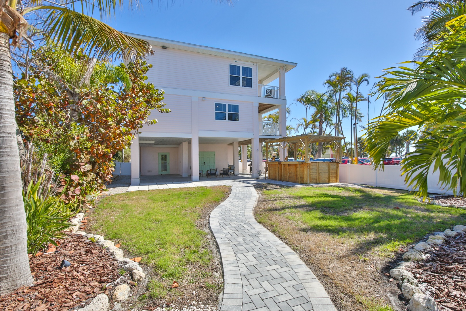 A charming tropical vacation home with palm trees and landscaped walkway leading to the entrance.