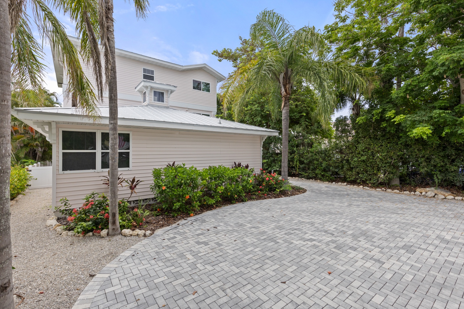 Charming two-story vacation home featuring tropical landscaping with palm trees, lush gardens, and paved parking area.