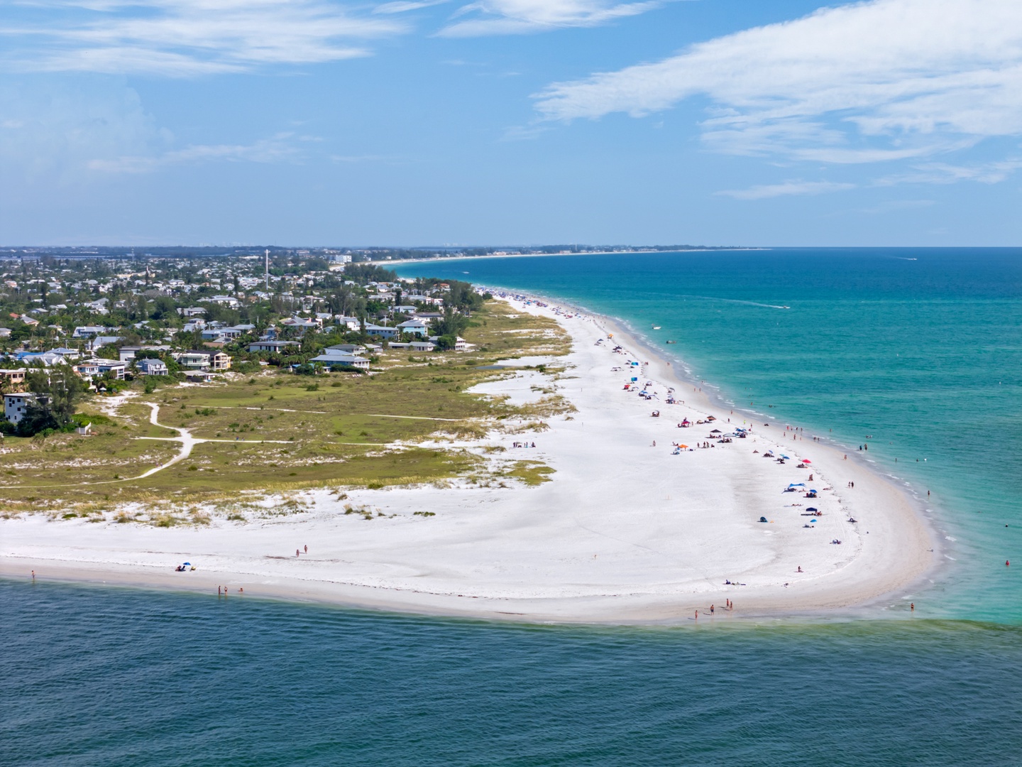 Stunning aerial view showcases pristine white sand beaches meeting turquoise waters, with residential areas nestled along this picturesque coastline.