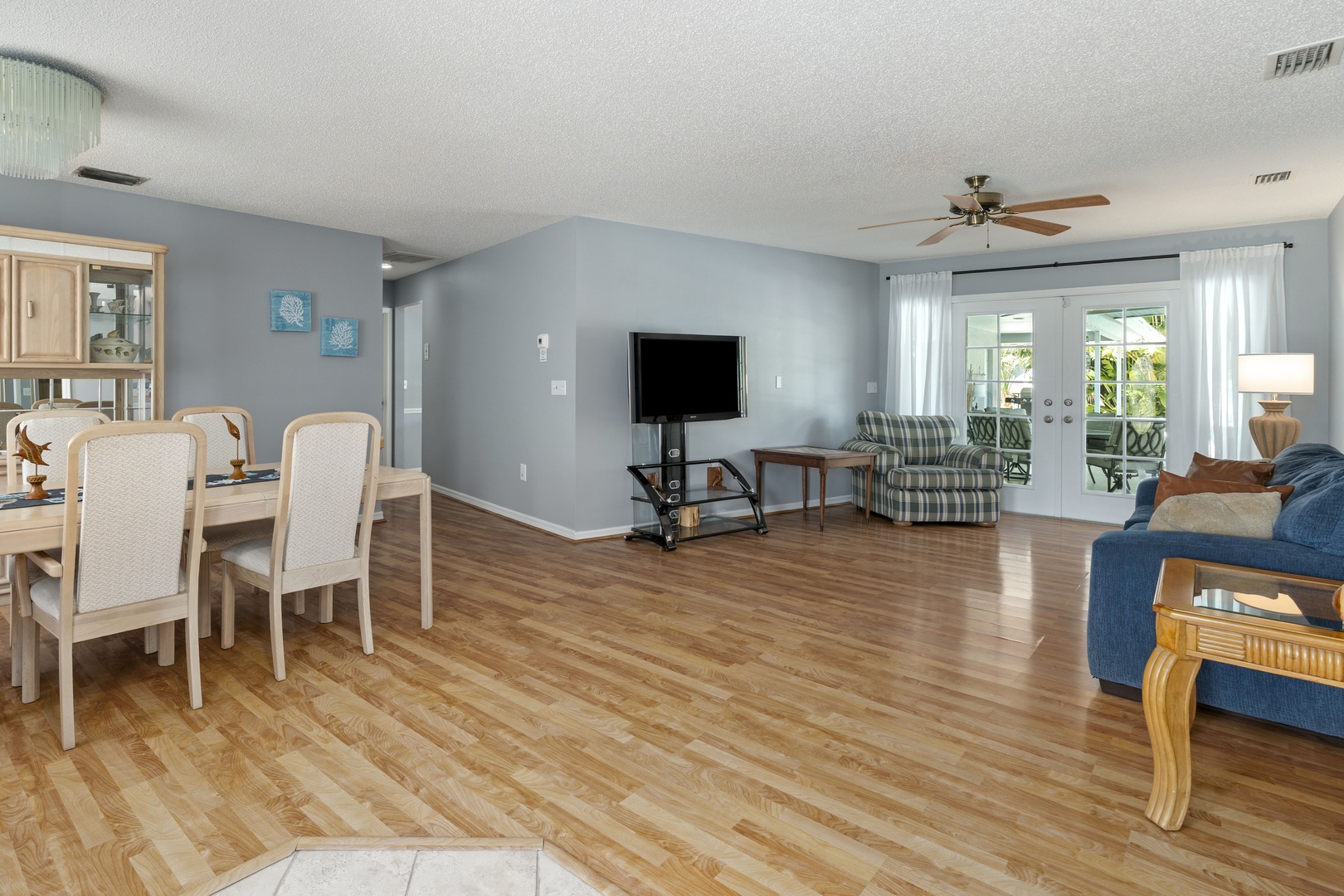 Step into your spacious open-concept living area, where warm wood floors flow seamlessly from the dining table to the cozy living room. Glass doors flood the space with natural light and open to your private outdoor retreat.