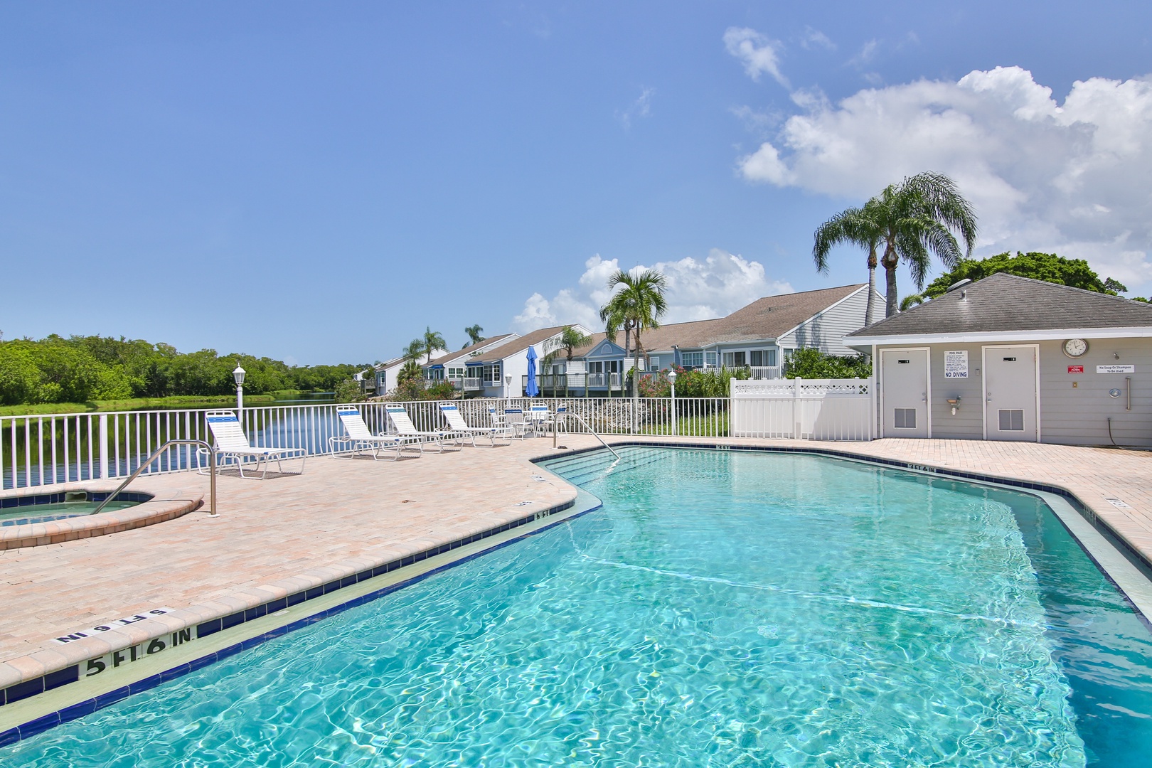 A sparkling pool area with crystal-clear water, surrounded by tropical palms and views of the lush surrounding area and residential community under sunny skies.
