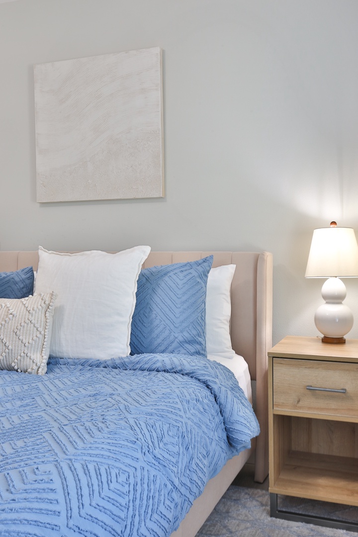 Sink into your serene bedroom sanctuary with soft blue bedding and warm lamp light creating the perfect ambiance for restful nights.
