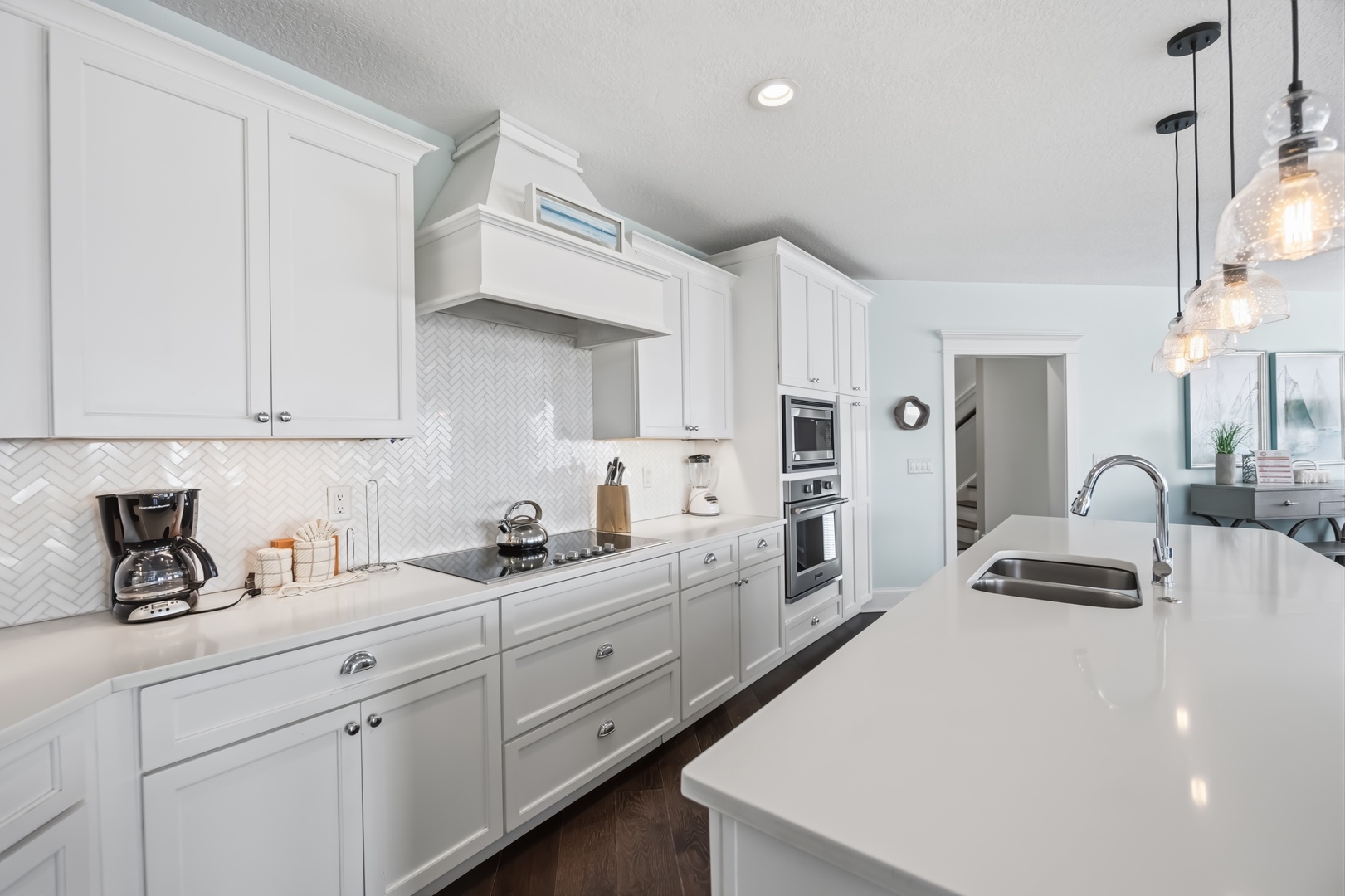 Your culinary dreams come alive in this pristine white kitchen featuring gleaming countertops, modern appliances, and elegant pendant lighting.