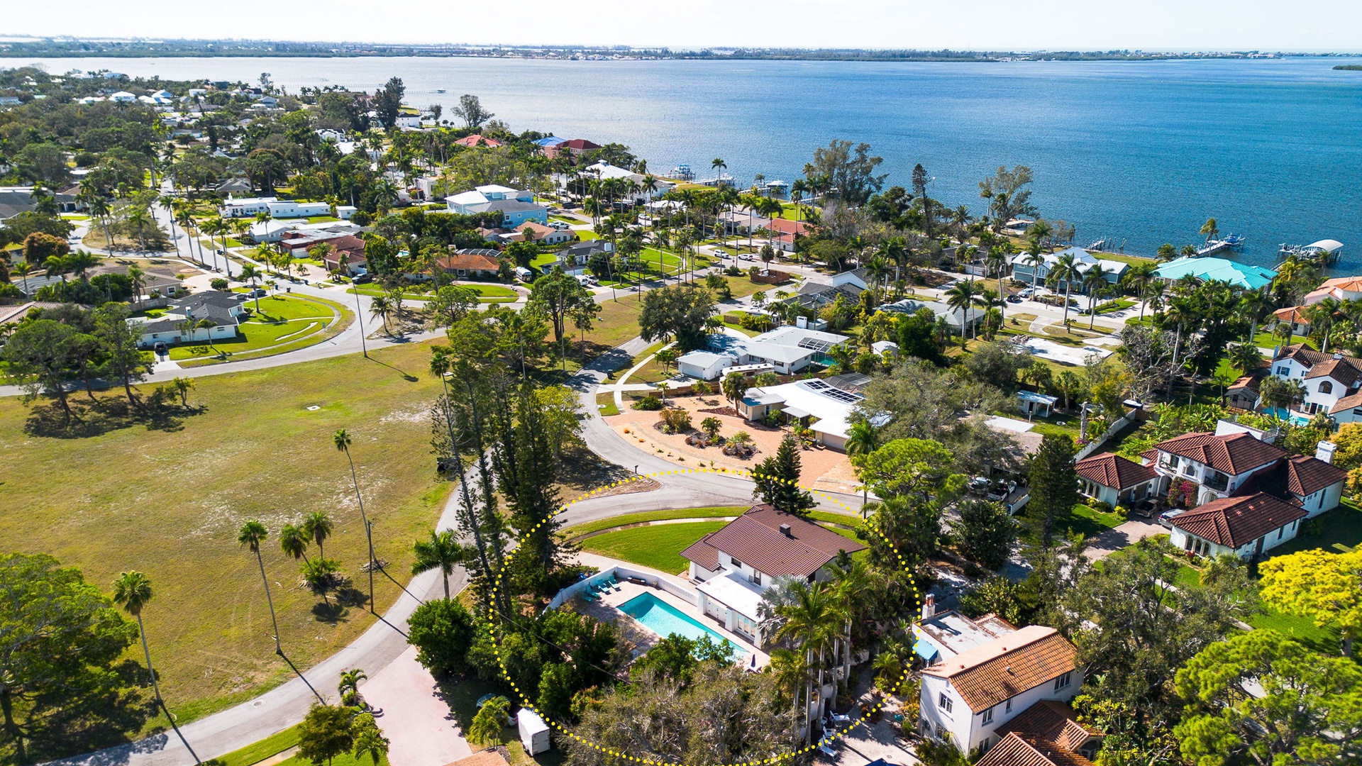 Aerial view of waterfront neighborhood with tree-lined streets and homes nestled near pristine blue waters and marina facilities.