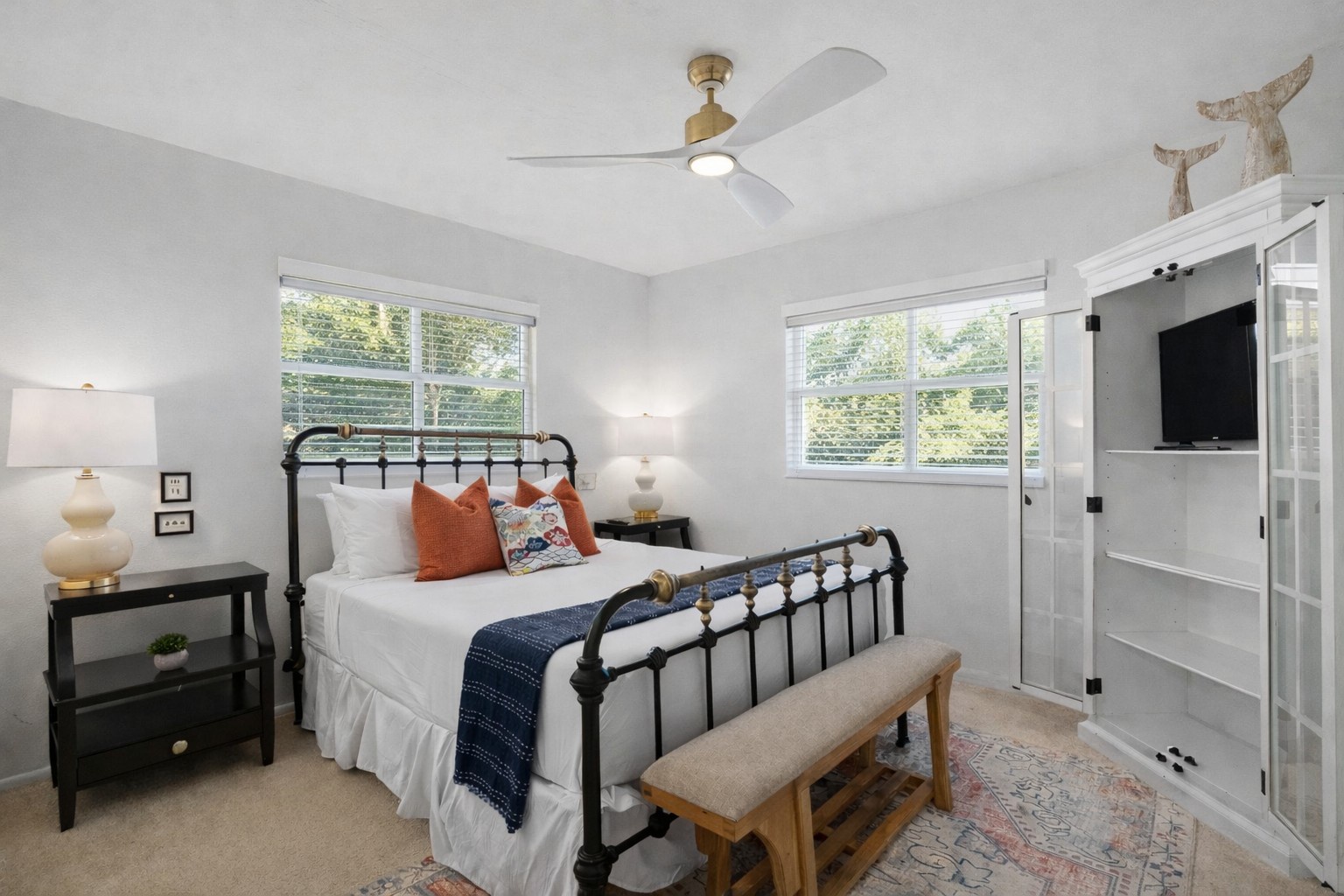 Your bright bedroom features a comfy iron bed, ceiling fan, and peaceful tree views through dual windows.