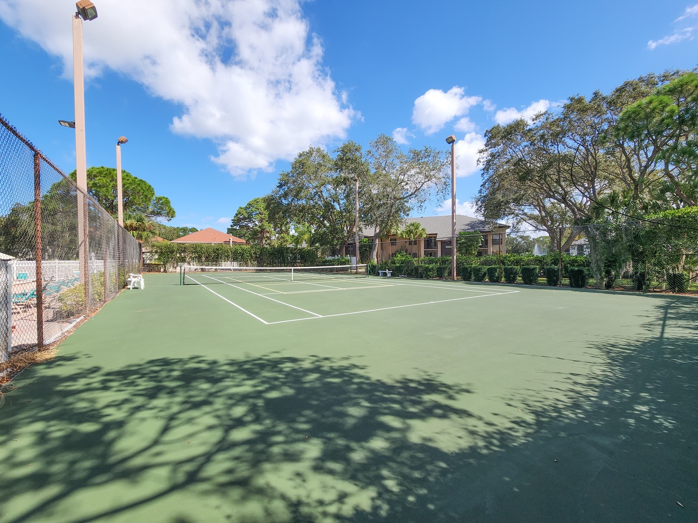 Full-sized tennis court with professional lighting surrounded by lush trees and residential buildings.
