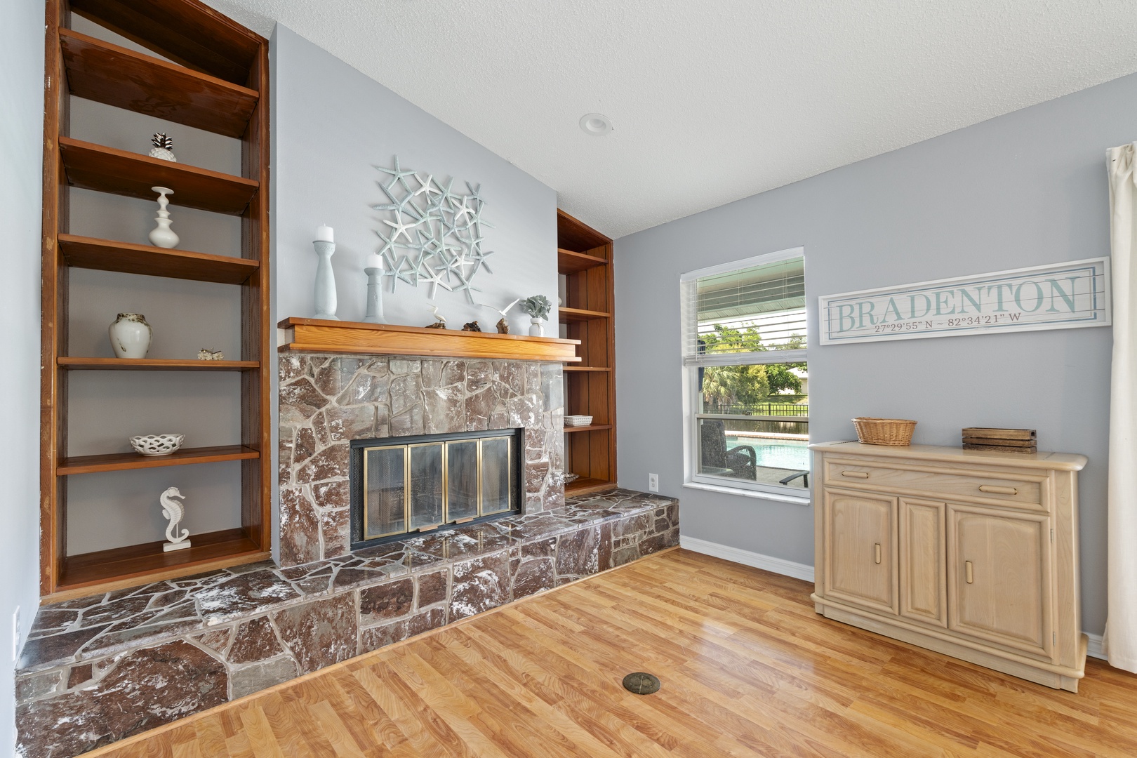 Unwind in your living room, where natural light streams through the window and a handsome stone fireplace creates a warm focal point for relaxing evenings.