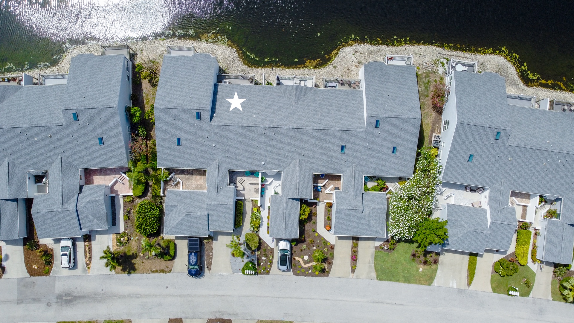 Aerial view of a modern waterfront townhome community with lake access, landscaped yards, private driveways, and serene natural surroundings.