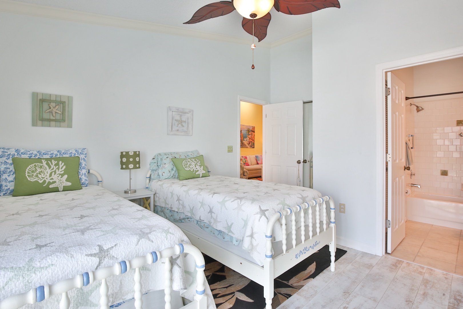 Rest easy in this coastal-inspired bedroom featuring two comfortable beds with beach-themed linens, a tropical ceiling fan, and an ensuite bathroom for your convenience.