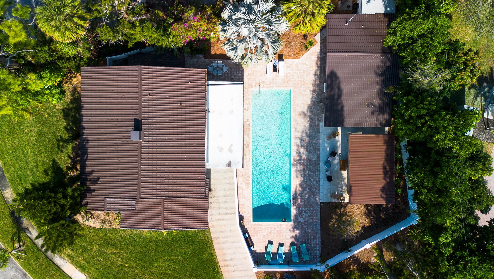 Aerial view of a modern vacation rental featuring a pristine swimming pool surrounded by tropical landscaping and lush greenery.