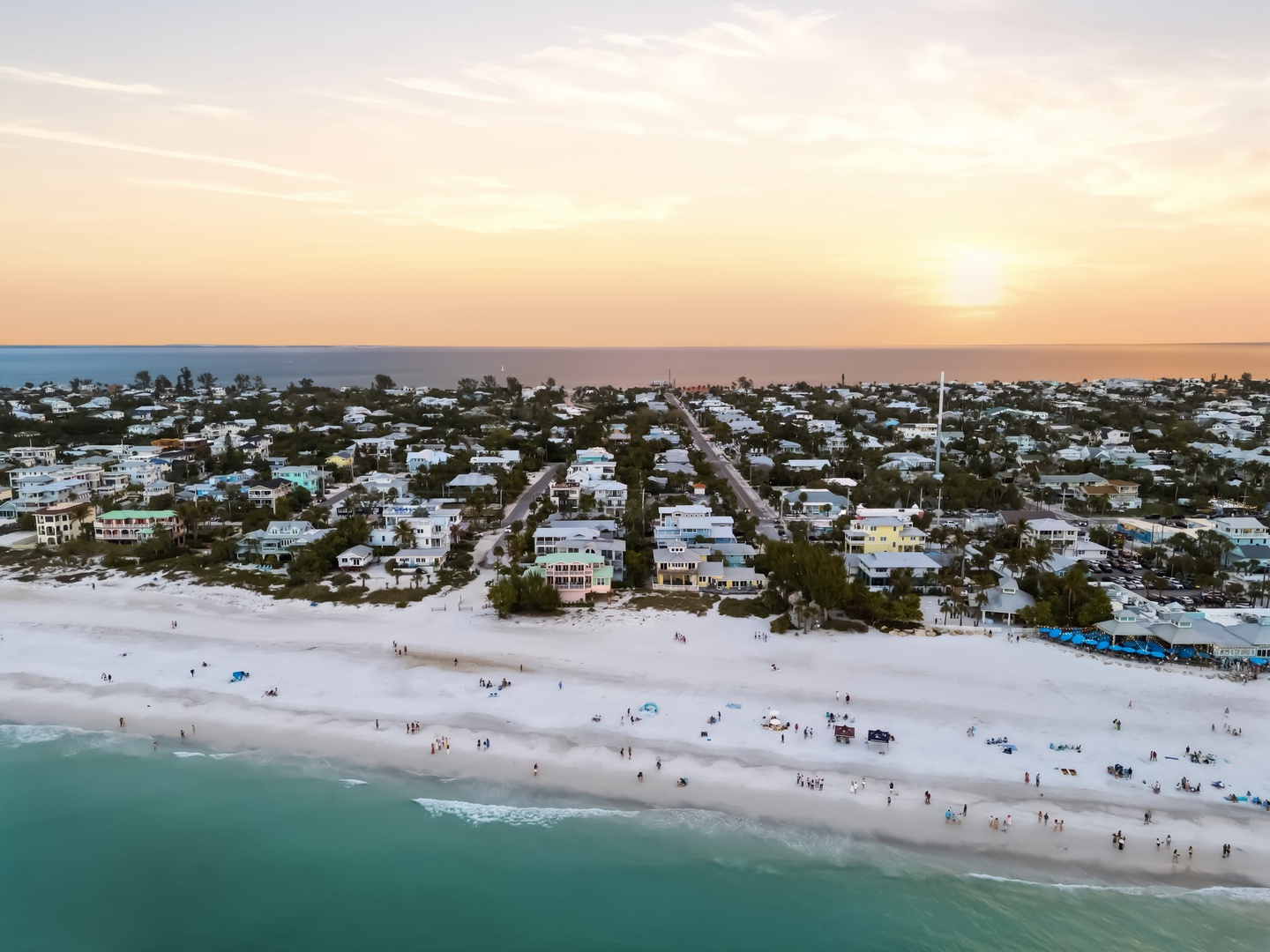Stunning aerial view of a pristine beachfront community at sunset, with white sand beaches and turquoise waters stretching along the coastline.