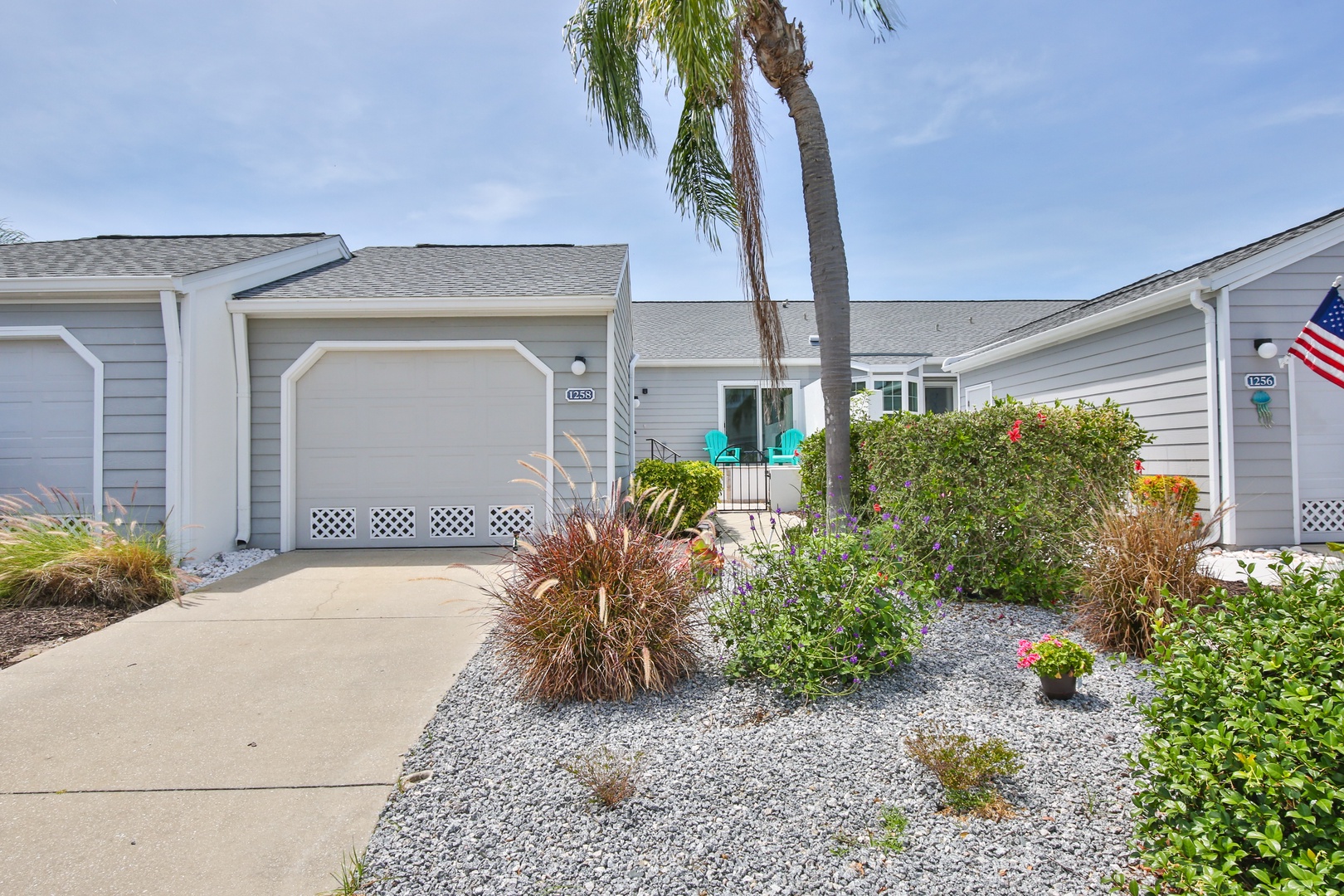 Charming coastal property entrance with inviting landscaping, palm tree, and garage parking. Located in a peaceful beach community setting.