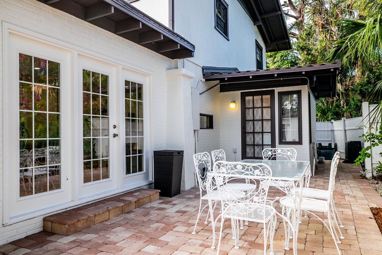 Unwind on your private brick patio featuring elegant white furniture, perfect for morning coffee or evening dining surrounded by lush tropical greenery.