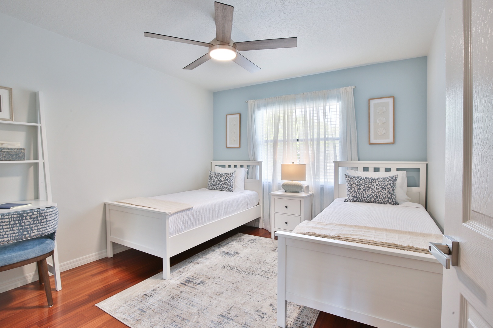Relax in your bright twin bedroom with comfortable beds, soothing blue accent wall, and gentle ceiling fan.