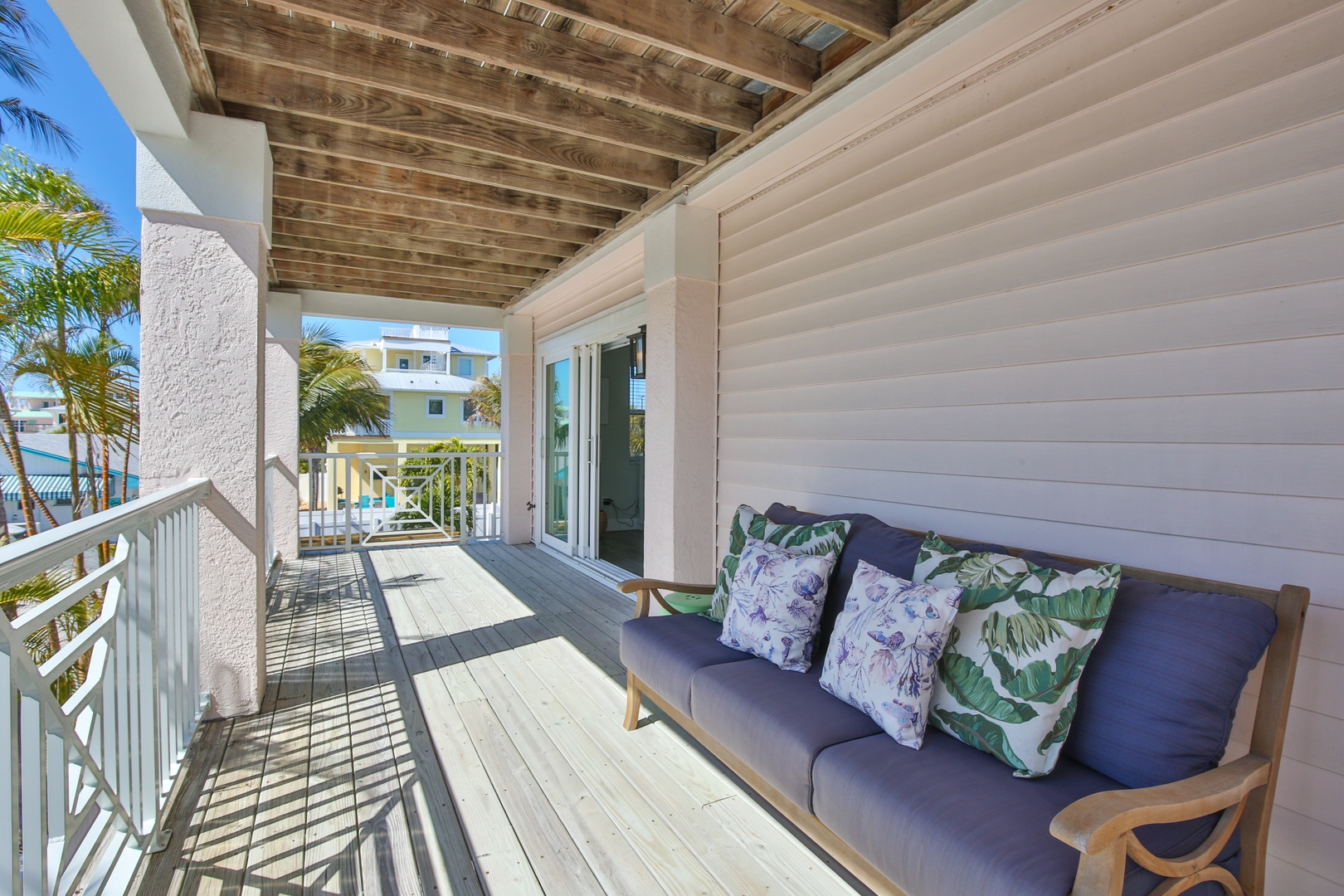 Relax on your private covered balcony with tropical-print cushions while palm trees sway nearby and colorful coastal homes dot the view.