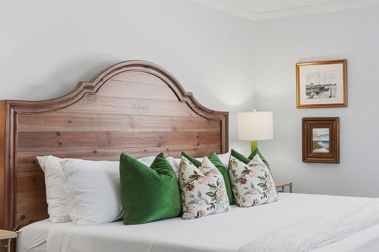 Sink into crisp white linens and vibrant green pillows beneath this rustic wood headboard, where coastal charm meets comfort.