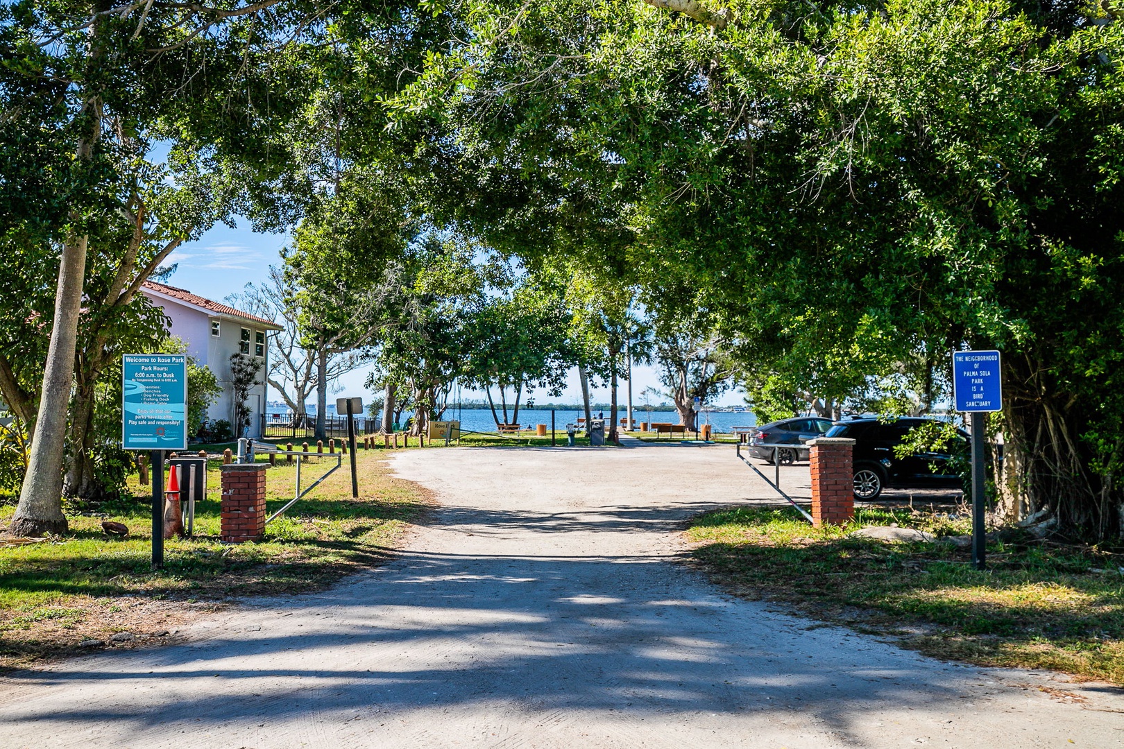 Tree-lined entrance to beachfront property with informational signage and glimpses of the sparkling waterfront beyond.