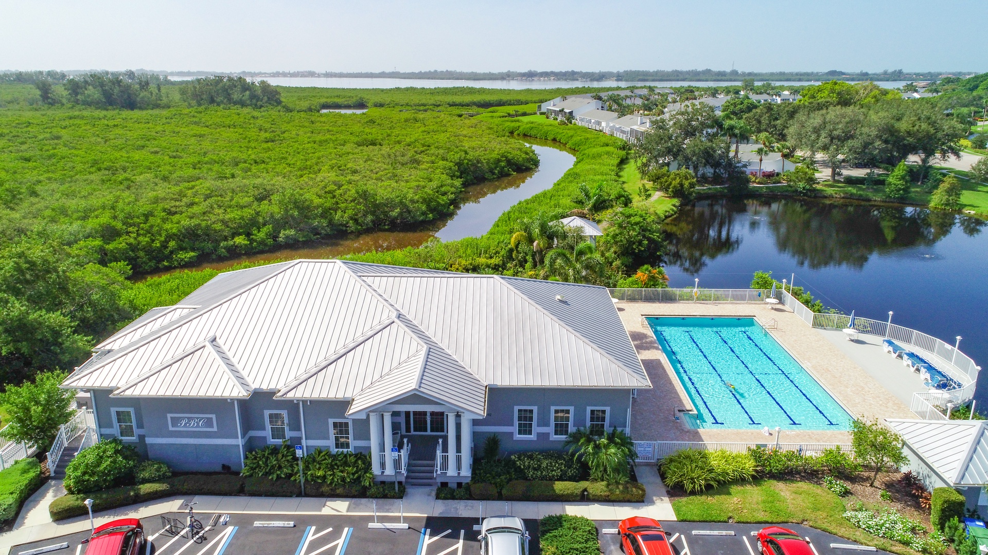 Aerial view of the property featuring an outdoor lap pool beside winding waterways and lush natural preserves, offering a peaceful setting surrounded by greenery.
