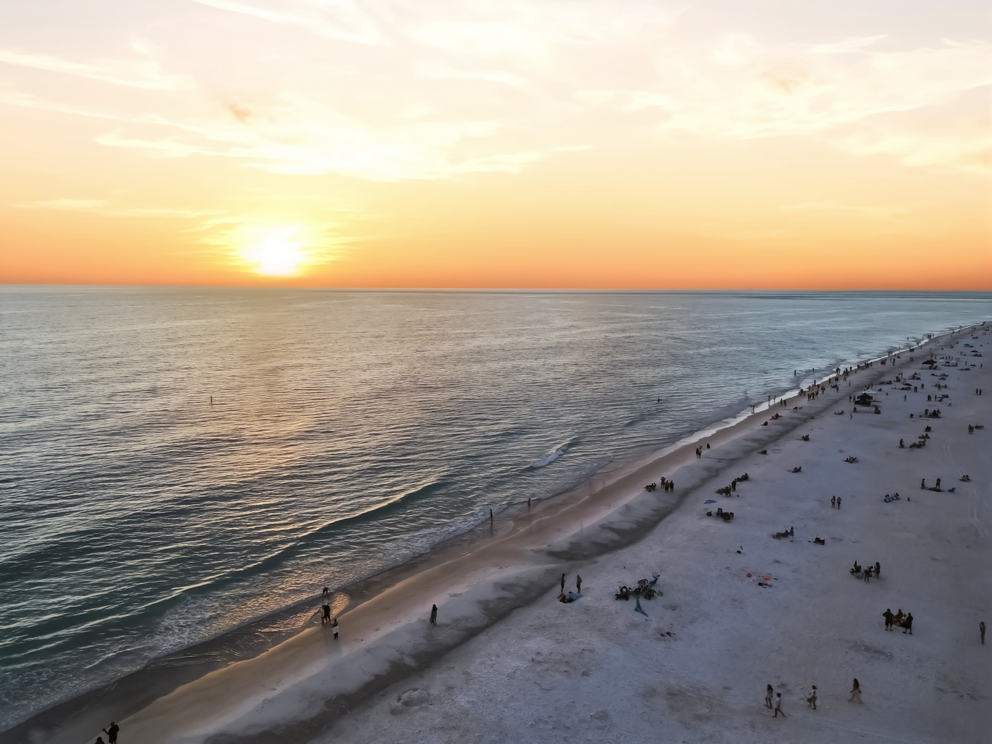Spectacular sunset paints the sky in golden hues over pristine sandy shores, where beachgoers gather to enjoy the evening coastal atmosphere.