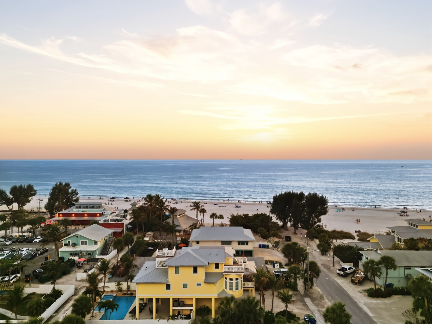 Aerial view of colorful beachfront properties with white sand beach and ocean stretching to the horizon at sunset.