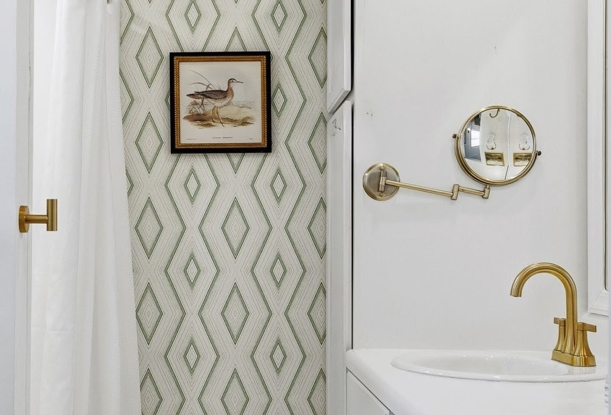 Freshen up in your elegantly designed bathroom with striking geometric wallpaper, brass fixtures, and thoughtful details that create a sophisticated retreat.