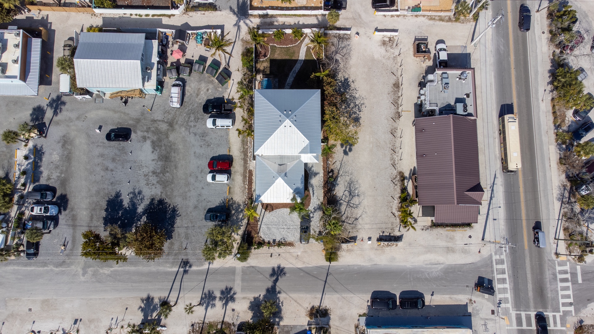 Aerial view of beachside properties with parking areas and palm trees lining quiet residential streets in a coastal neighborhood.