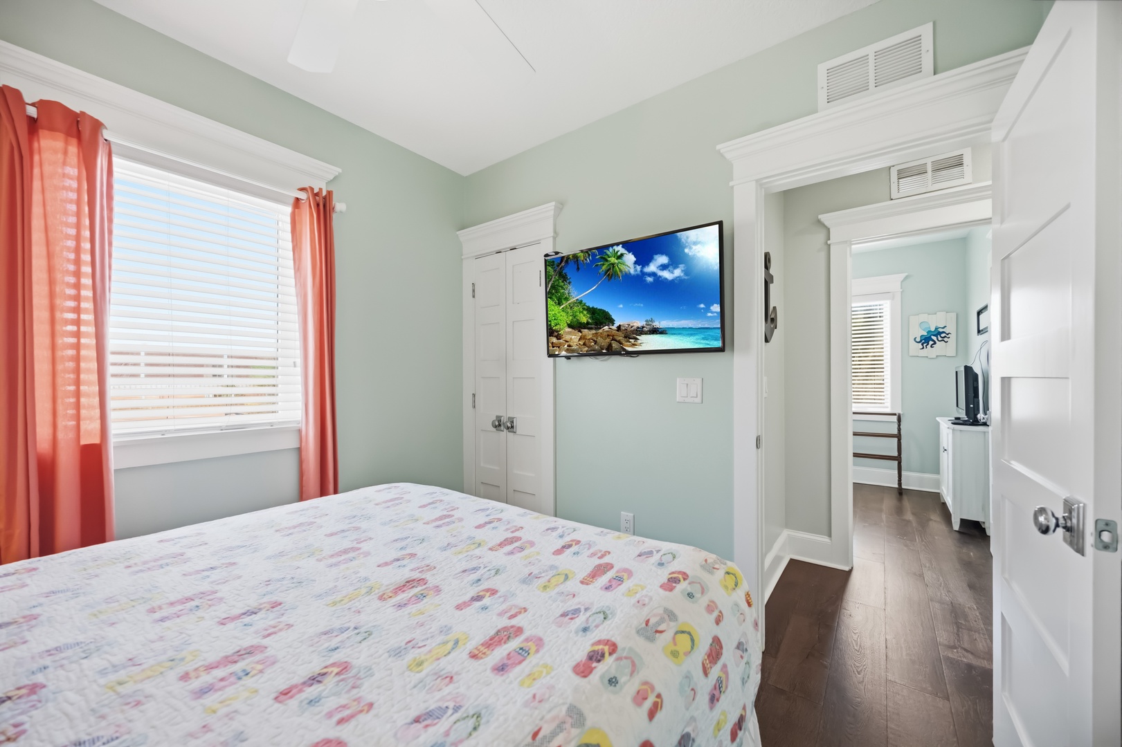 Your peaceful bedroom features a cozy bed, flatscreen TV, and bright coral curtains that add tropical charm to your restful retreat.