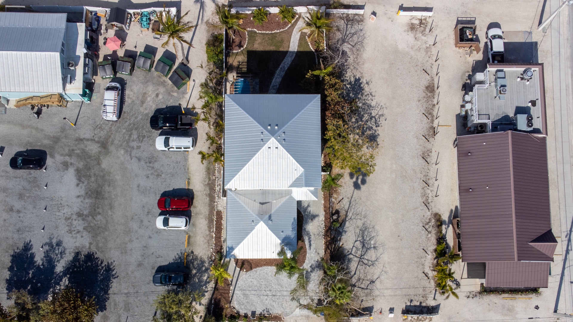 Aerial view showcasing the property's distinctive white roofline and prime beachside location with convenient parking and tropical surroundings.