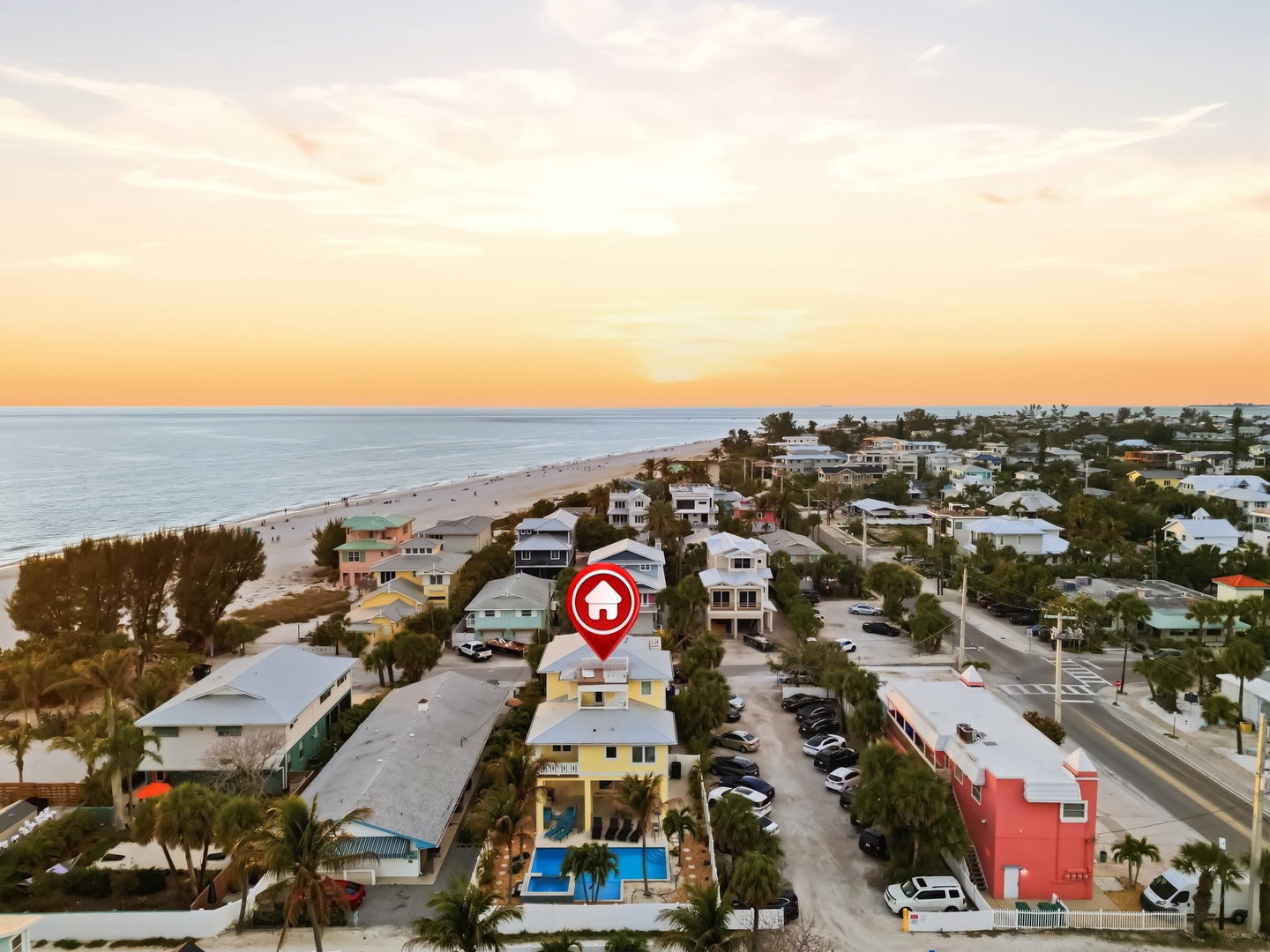Aerial view shows a beachfront community at sunset with coastal homes and the property location marked near the shore.