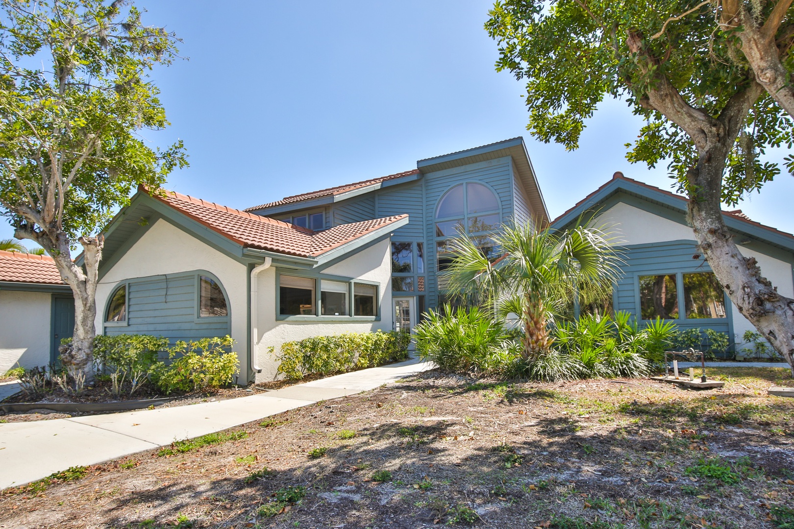 Modern vacation home with tropical landscaping and distinctive architecture set among mature trees in a peaceful residential setting.