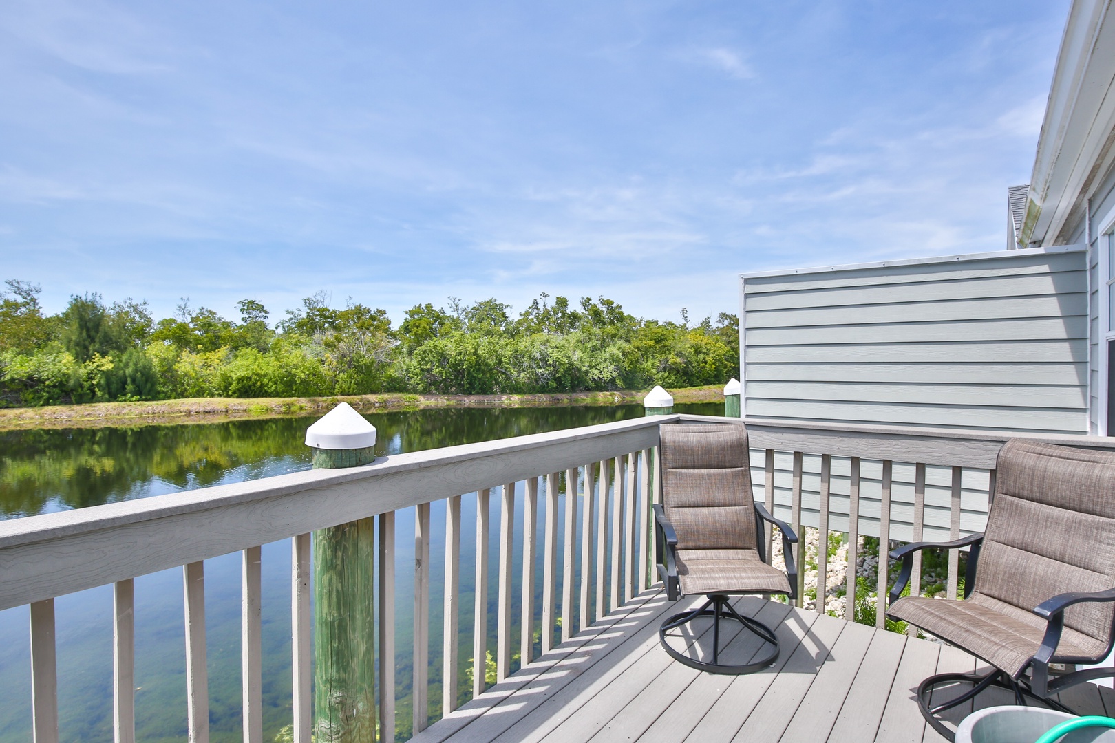 Unwind in comfortable chairs on the deck overlooking a tranquil waterway surrounded by lush greenery—your perfect spot to soak in the peaceful scenery.