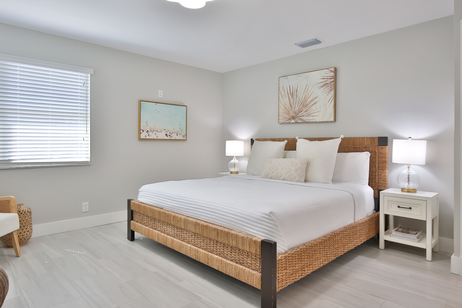 Sink into crisp white linens on your woven rattan bed, where coastal artwork and warm lighting create the perfect retreat for restful nights.