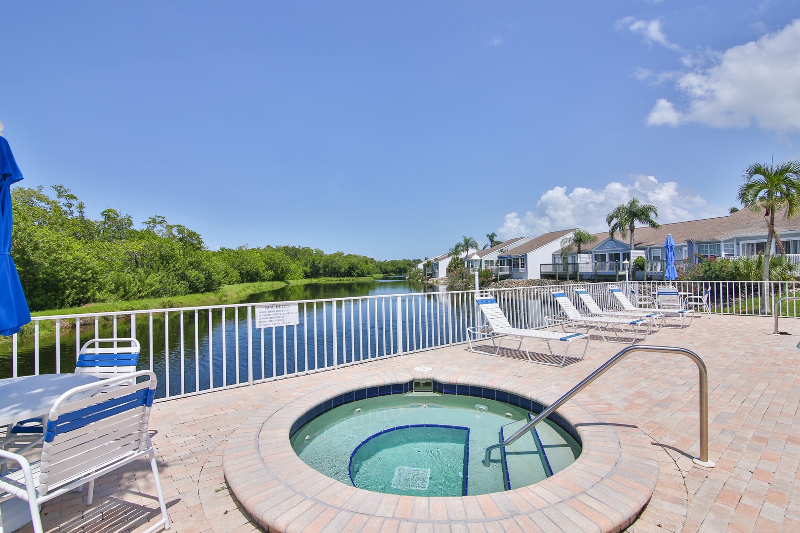 Soak in the bubbling hot tub while taking in serene water and lush greenery views under a bright blue sky—your perfect spot to unwind.