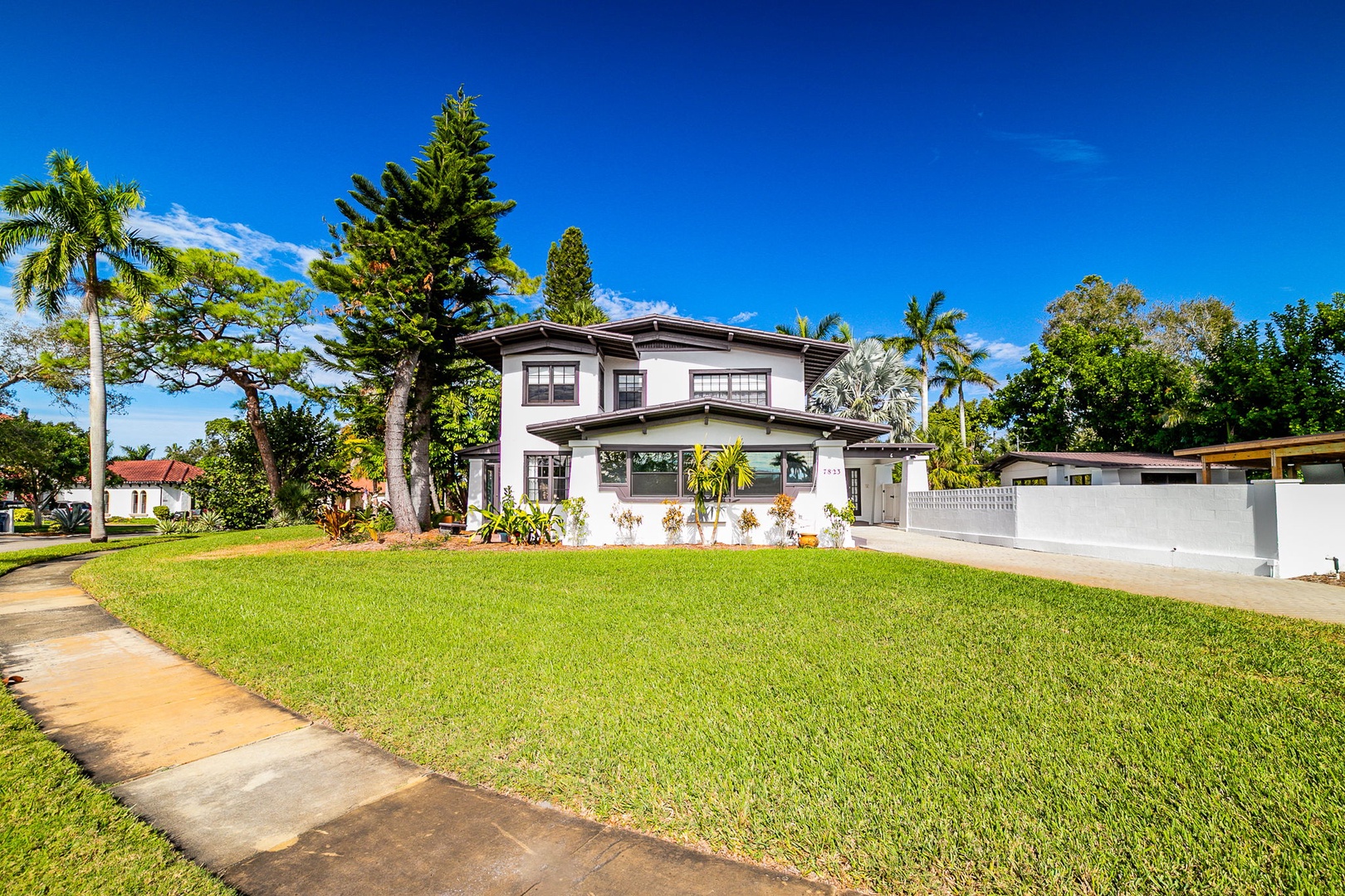 A charming two-story property nestled among tropical palms and lush greenery under brilliant blue skies.