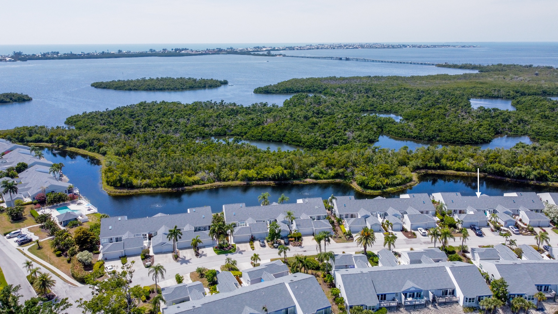 Aerial view captures a coastal residential community bordered by lush mangrove islands and tranquil waterways leading to the open bay beyond.