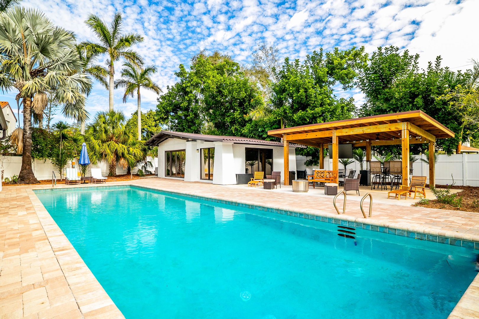 Your private tropical oasis awaits with a sparkling pool surrounded by swaying palms and covered outdoor dining.